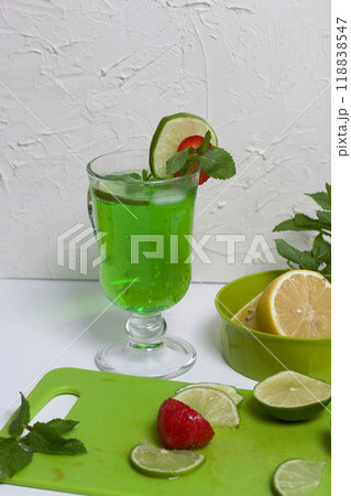 Green lemonade in a glass. Decorated with lime and strawberries. With sprigs of mint. Near lemon and mint. Green lemonade in a glass. Decorated with lime and strawberries. With sprigs of mint. Near lemon and mint. 118838547