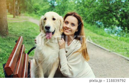Happy smiling owner woman with Golden Retriever dog sitting together on bench in summer park 118839792