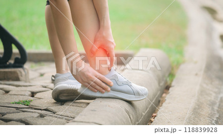 Sprained ankle problem. woman jogger. 30s asian female wearing sportswear holding her ankle with pain after running exercise in public park. Sprained ankle problem. woman jogger. 30s asian female wearing sportswear holding her ankle with pain after running exercise in public park. 118839928