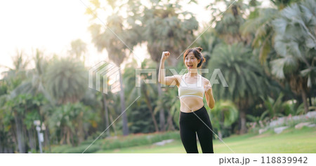 Happy fitness woman achieve goal, finish marathon with hands up, celebrating victory while jogging, triumphing in park 118839942
