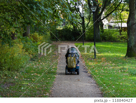 A woman in a wheelchair is driving along the road to the parks. 118840427