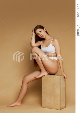 Perched on wooden block, model's thoughtful pose and casual stance bring balance of elegance and simplicity against beige background. 118840727