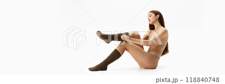 Banner. Adjusting socks, woman sits gracefully, combining casual comfort with elegance against white studio background with copy space. 118840748