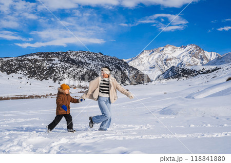 Mom and son running on a snow-covered slope against the backdrop of a mountain landscape in winter 118841880