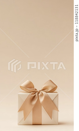 Golden gift box with a satin ribbon bow on a beige background. Perfect for Christmas, New Year's, or holiday gift concepts. 118842131