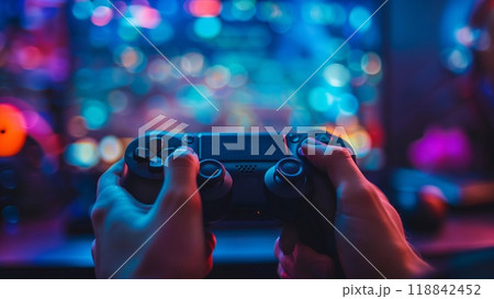 Hands gripping a gaming controller, fully focused on an engaging online game with bright, colorful lights illuminating the room Hands gripping a gaming controller, fully focused on an engaging online game with bright, colorful lights illuminating the room 118842452