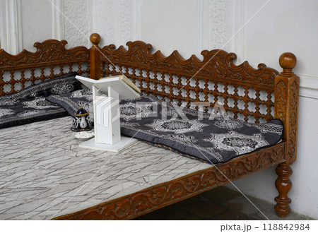 Traditional Central Asian carved wooden cot with book stand and kettle in Samarkand, Uzbekistan 118842984