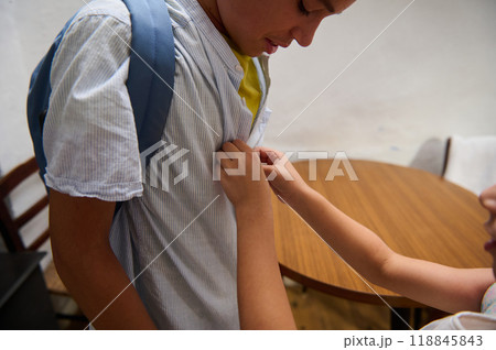 Child helping a peer with a school backpack indoors Child helping a peer with a school backpack indoors 118845843