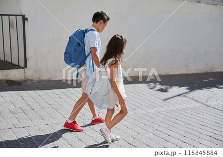 Children walking to school with backpacks under sunny skies Children walking to school with backpacks under sunny skies 118845884