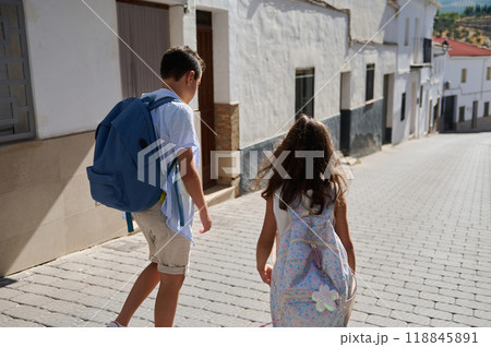 Children with backpacks walking down a sunny street Children with backpacks walking down a sunny street 118845891