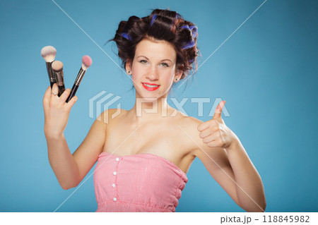 woman in hair rollers holds makeup brushes 118845982