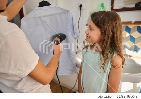 Young girl observes shirt being steamed at home Young girl observes shirt being steamed at home 118846058