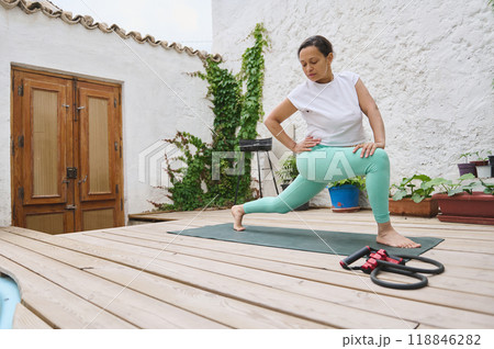 Woman practicing yoga on a wooden deck in an outdoor setting with plants and a serene atmosphere Woman practicing yoga on a wooden deck in an outdoor setting with plants and a serene atmosphere 118846282