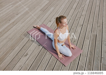 High angle shot of young Caucasian woman dressed in comfortable sportswear sitting in half pigeon position on dusty pink mat 118846895