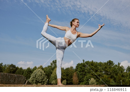 Low angle shot of young Caucasian woman dressed in fashionable and comfy sportswear practicing dancer pose in park 118846911