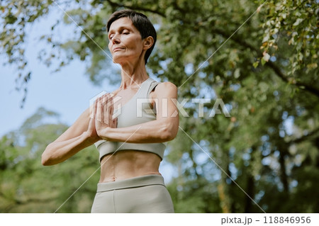 Low angle shot of sporty retired Caucasian woman relaxing while standing in yoga position on summer day in park 118846956