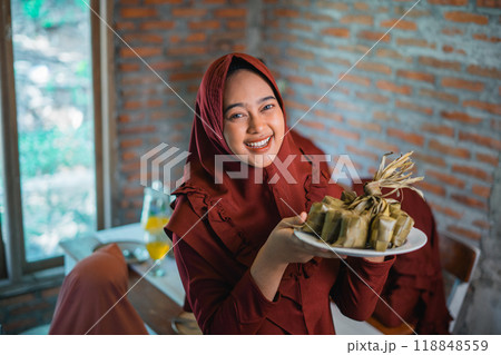 Attractive mother in headscarf showing ketupat for Eid Attractive mother in headscarf showing ketupat for Eid 118848559