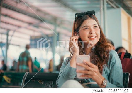 A Smiling Young Woman Using Her Smartphone in a Modern Airport Lounge Environment A Smiling Young Woman Using Her Smartphone in a Modern Airport Lounge Environment 118851101
