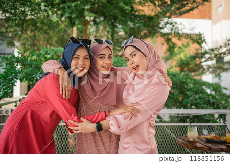 In a stunning natural environment, friends dressed in vibrant outfits share warm embraces In a stunning natural environment, friends dressed in vibrant outfits share warm embraces 118851156