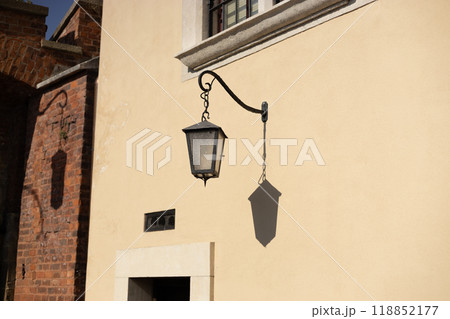 Old antique metal lamp at the old wall. Victorian vintage street lantern at the day time, turned off. The wall lamp on the old street 118852177