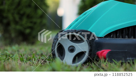 Man cuts the grass in the backyard with an electric lawnmower. Gardener mowing grass with lawn mower. Man cuts the grass in the backyard with an electric lawnmower. Gardener mowing grass with lawn mower. 118852525