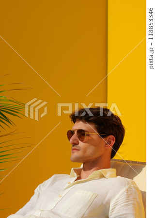 Vertical poster of a young man in a lounge chair against a bright yellow patio wall in a home hotel, vacation advertising concept 118853346