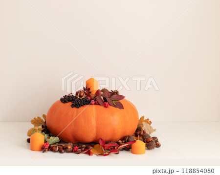 A large pumpkin with candles and autumn decorations on white table with copy space. Thanksgiving day concept. Autumn leaves, berries, acorns and chestnuts. A large pumpkin with candles and autumn decorations on white table with copy space. Thanksgiving day concept. Autumn leaves, berries, acorns and chestnuts. 118854080