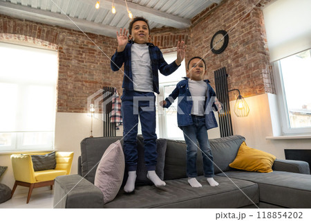 Cheerful kids jumping on sofa at home Cheerful kids jumping on sofa at home 118854202