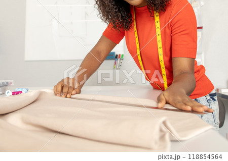 Dressmaker in orange tshirt tailoring fabric for a new dress Dressmaker in orange tshirt tailoring fabric for a new dress 118854564