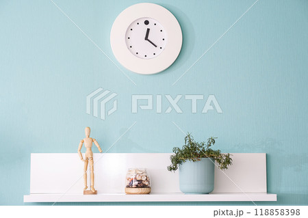 Minimalist interior with clock, puppet, and potted plant on white shelf. 118858398