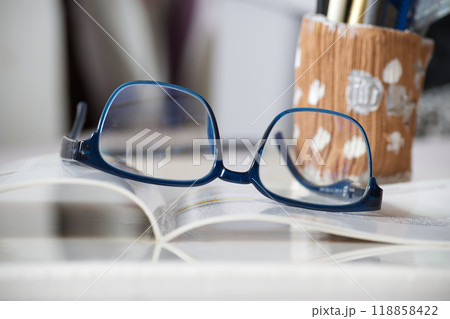 Blue reading glasses resting on an open book in a cozy study environment Blue reading glasses resting on an open book in a cozy study environment 118858422