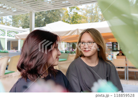 Cheerful female companions casually chatting and sharing a lighthearted moment while waiting for their order at a cozy summer coffee shop, capturing the fun and carefree spirit of friendship 118859528