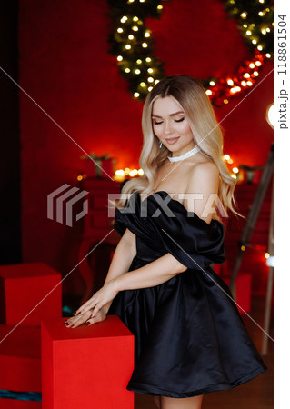 Blonde woman in black dress posing for photo in front of Christmas tree Blonde woman in black dress posing for photo in front of Christmas tree 118861504