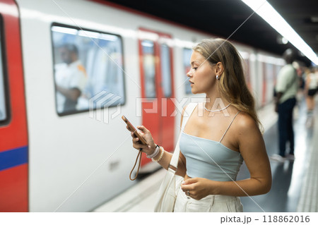Young woman with phone stands at metro station 118862016