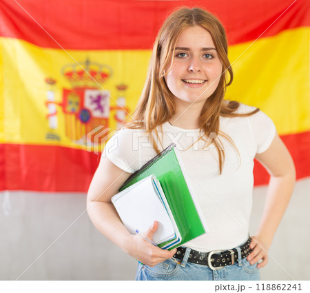 Portrait of a smiling satisfied girl student with notebooks in her hands against the background of flag of Spain Portrait of a smiling satisfied girl student with notebooks in her hands against the background of flag of Spain 118862241
