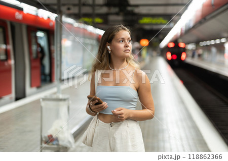 Young girl standing in platform holding phone with wireless headphones on airs 118862366