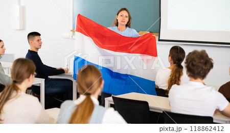Adult female teacher showing the flag of the Netherlands to students 118862412