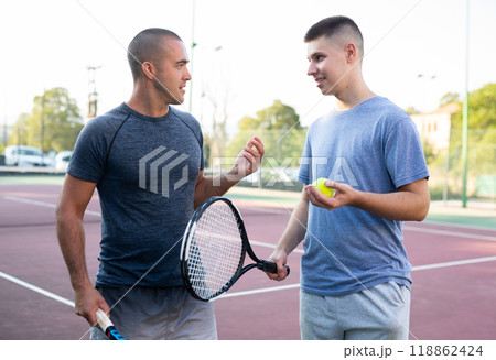Two men with rackets in their hands chatting after playing on tennis court 118862424