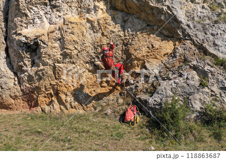 Aerial view of mountain rescuer abseiling on a rocky wall hanging on a rope Aerial view of mountain rescuer abseiling on a rocky wall hanging on a rope 118863687