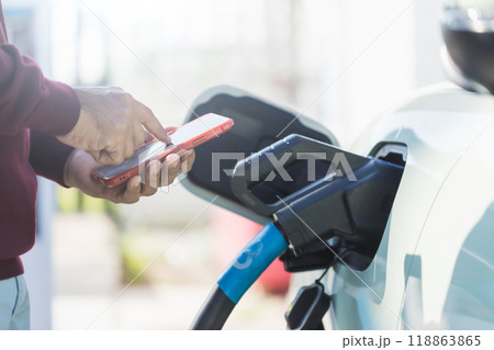 Idea of using electric cars. An electric car user is using smartphone to control recharge an electric car in station. The use of electric cars as the latest alternative energy source in Thailand. Idea of using electric cars. An electric car user is using smartphone to control recharge an electric car in station. The use of electric cars as the latest alternative energy source in Thailand. 118863865