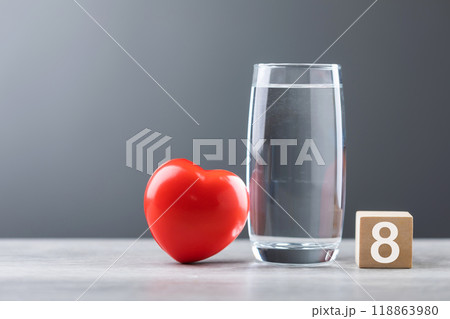 Glass of water and a red heart are placed on a table, symbolizing the concept of drinking water for better health. Hydration for maintaining a healthy heart and overall well-being 118863980