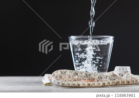 Glass of water and a measuring tape are placed on a table, symbolizing the concept of drinking water for weight loss and better health. Importance of hydration for both fitness and overall wellness 118863981