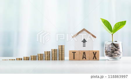 TAX is write on a wooden block next to a stack of coins and a house model and coins jar with small plant on a wooden table. Tax awareness, financial planning, savings, and effective money management TAX is write on a wooden block next to a stack of coins and a house model and coins jar with small plant on a wooden table. Tax awareness, financial planning, savings, and effective money management 118863997