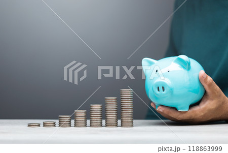 Man is dropping coins into a blue piggy bank, symbolizing the act of saving and financial responsibility. Financial planning, budgeting, and building a stable future through consistent savings Man is dropping coins into a blue piggy bank, symbolizing the act of saving and financial responsibility. Financial planning, budgeting, and building a stable future through consistent savings 118863999