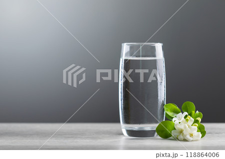 Glass of cold water sits on a table with a dark, blurred grey background. The image evokes freshness and simplicity, highlighting hydration and refreshment. 118864006