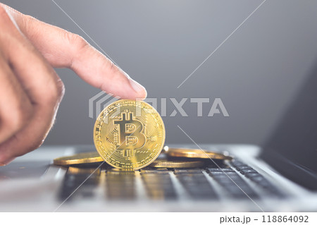 Man holds a golden Bitcoin while using a laptop, representing Bitcoin as a form of digital currency for online transactions, highlighting the concept of modern financial technology and crypto usage 118864092