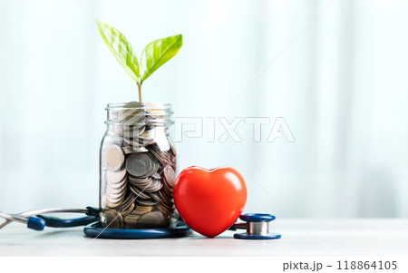 Savings concept for future healthcare. A jar filled with coins and a small plant in the center, accompanied by a heart and a stethoscope, symbolizing saving money for good health in the future 118864105