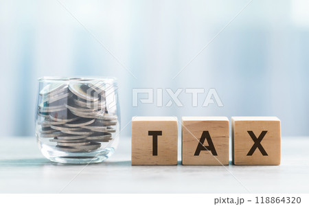 TAX is written on a wooden block beside a clear glass coins jar on a wooden table against a bright white background. Tax and Financial planning, savings, and wise money management. TAX is written on a wooden block beside a clear glass coins jar on a wooden table against a bright white background. Tax and Financial planning, savings, and wise money management. 118864320