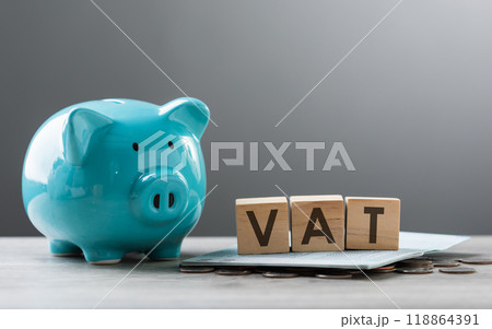 VAT is written on a wooden block, alongside a pile of coins, a blue piggy bank, and a calculator, placed on a wooden table against a grey background. VAT, financial management, and budgeting. VAT is written on a wooden block, alongside a pile of coins, a blue piggy bank, and a calculator, placed on a wooden table against a grey background. VAT, financial management, and budgeting. 118864391