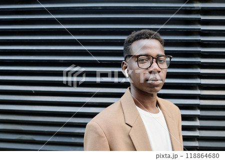 Young African American male manager wearing stylish eyeglasses standing against office building and looking at camera Young African American male manager wearing stylish eyeglasses standing against office building and looking at camera 118864680